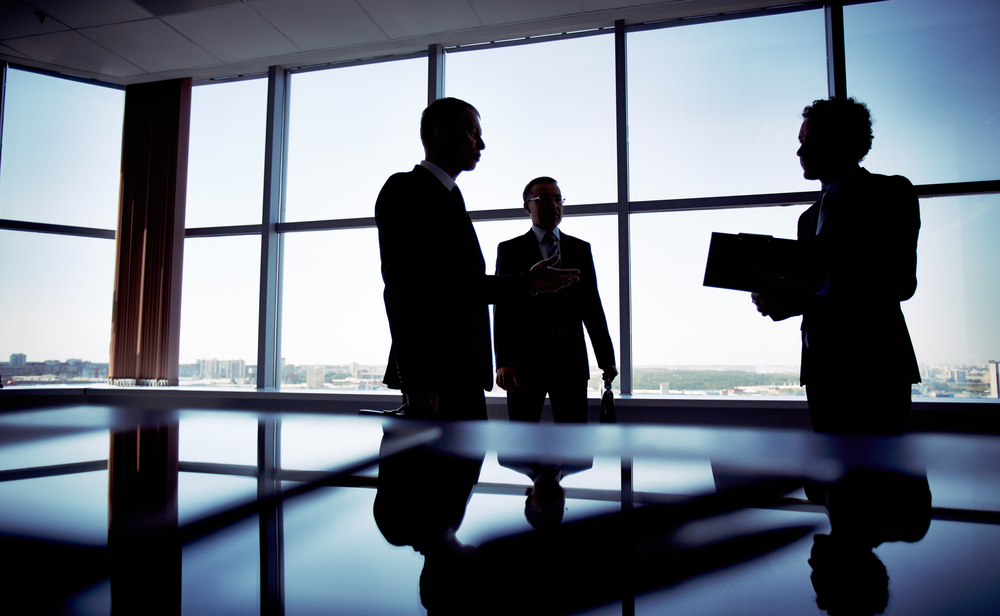 Three adults standing in conference room. 